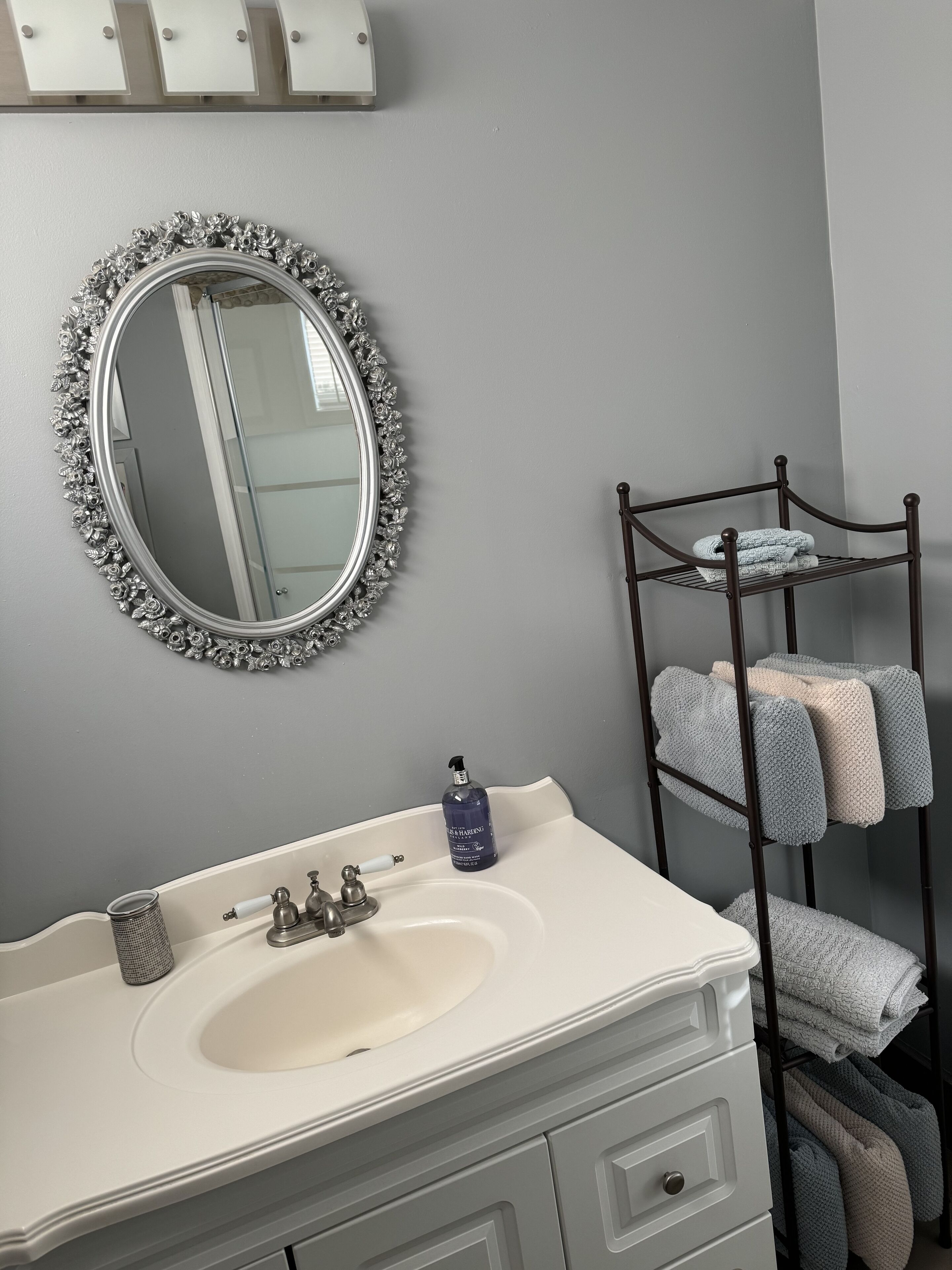 A bathroom with a white sink, a mirror with a floral frame, and a towel rack with folded towels.
