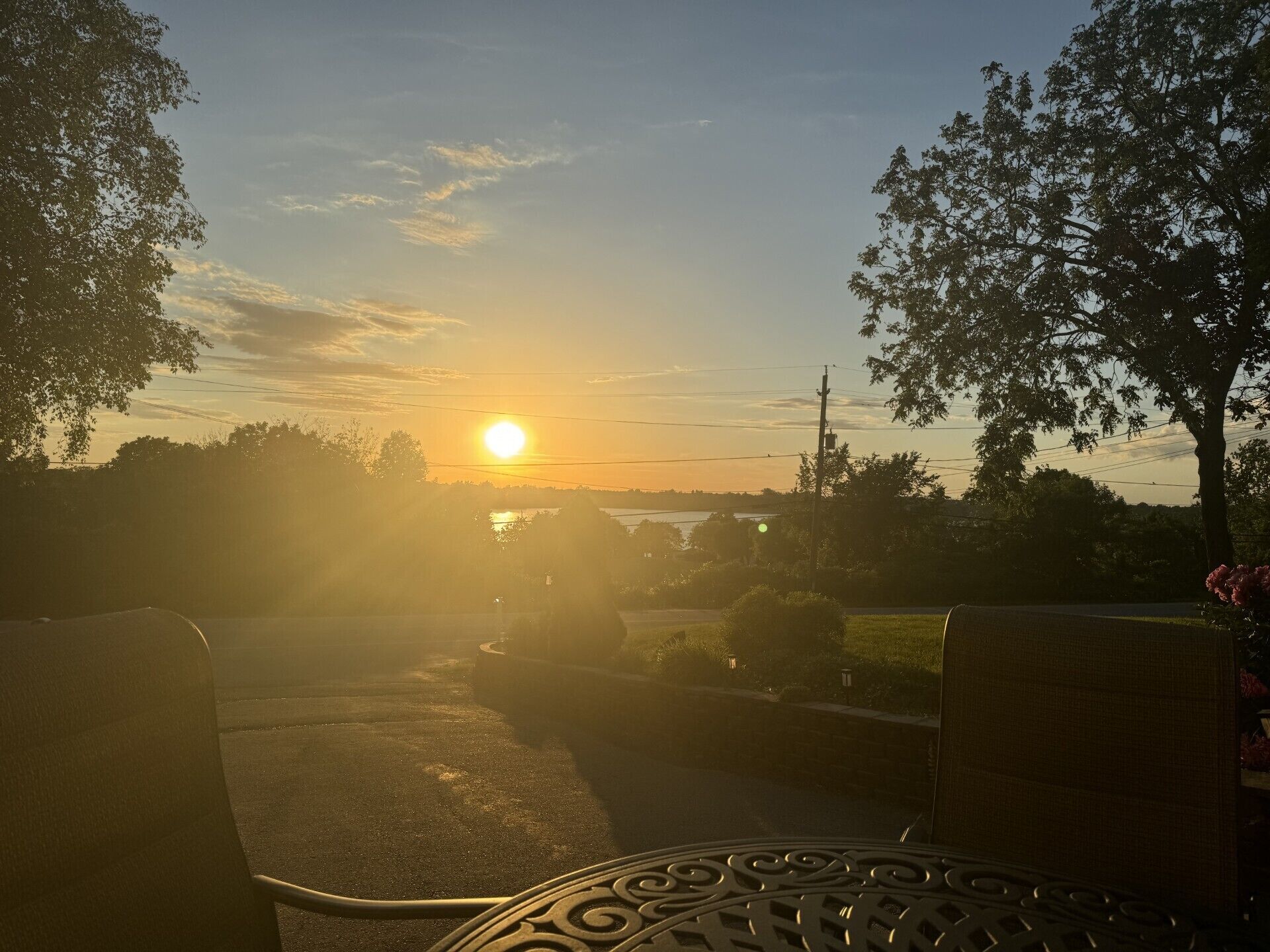 Tramonto visto da un balcone con ringhiera in metallo, che si affaccia su una strada e alberi.
