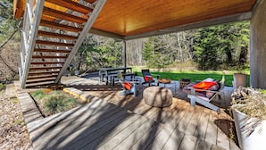 A covered outdoor deck with wooden flooring, a staircase, and outdoor furniture including chairs and a sofa. - Neal Creek Retreat - Urban Design, Gorgeous Rural Natural Surroundings (Hood River)