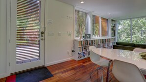 A modern interior with a wooden floor, white walls, a white dining table with chairs, a bookshelf, and a window with blinds. - Neal Creek Retreat - Urban Design, Gorgeous Rural Natural Surroundings (Hood River)