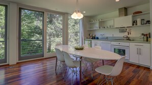 A modern kitchen with a large dining table, white cabinets, and a view of the outdoors. - Neal Creek Retreat - Urban Design, Gorgeous Rural Natural Surroundings (Hood River)