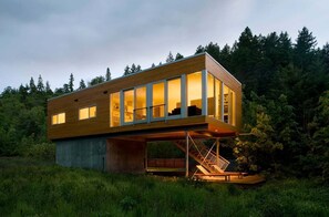 A modern house with a wooden exterior, large glass windows, and a staircase leading to an upper level.
