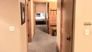 A narrow hallway with carpeted floors leading to a bedroom with a bed and a wooden wardrobe. - Creekside Condo w/ private hot tub at Boyne!  Ski-in/Ski-out, Golf, Bike, Swim  (Boyne Falls)