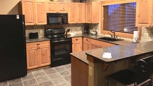A kitchen with wooden cabinets, a black refrigerator, a microwave, a stove, and a sink. - Creekside Condo w/ private hot tub at Boyne!  Ski-in/Ski-out, Golf, Bike, Swim  (Boyne Falls)