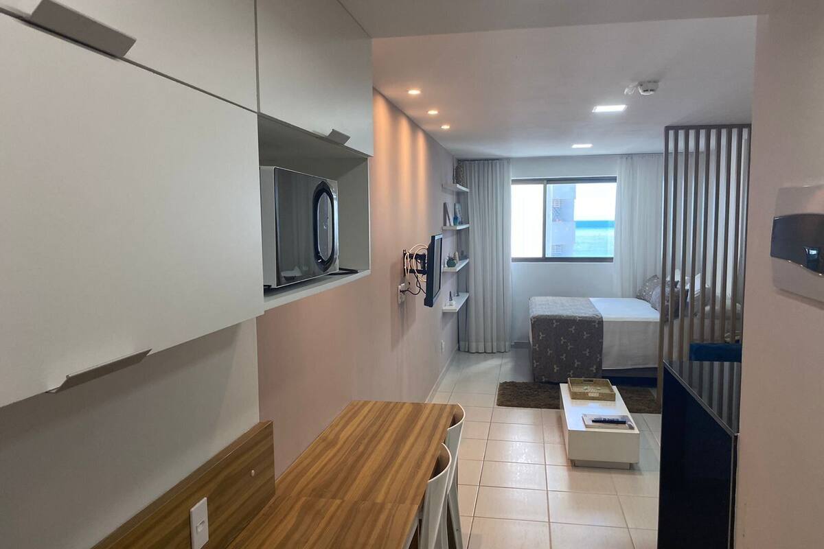 A compact hotel room with a kitchenette, a bed, a small table, and a window with a view.