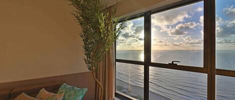 A room with a large window overlooking a body of water, a potted plant, and a sofa with patterned cushions.