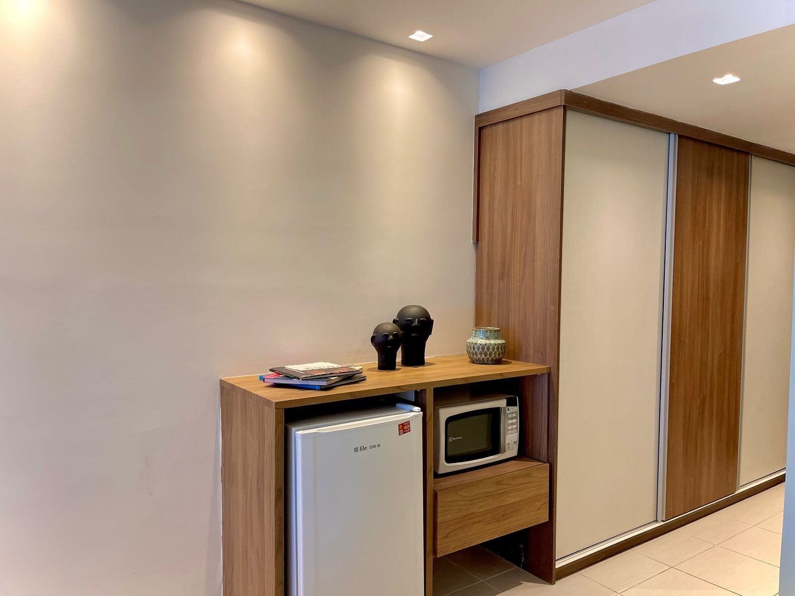 A compact kitchenette with a refrigerator, microwave, and wooden storage unit.