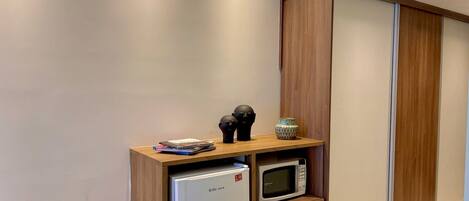 A compact kitchenette with a refrigerator, microwave, and wooden storage unit.