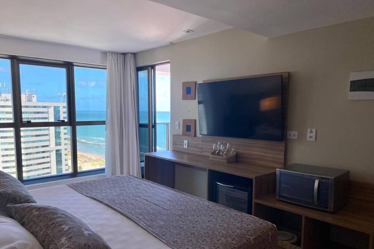A hotel room with a large bed, a TV, a desk with a computer, and a view of the ocean.