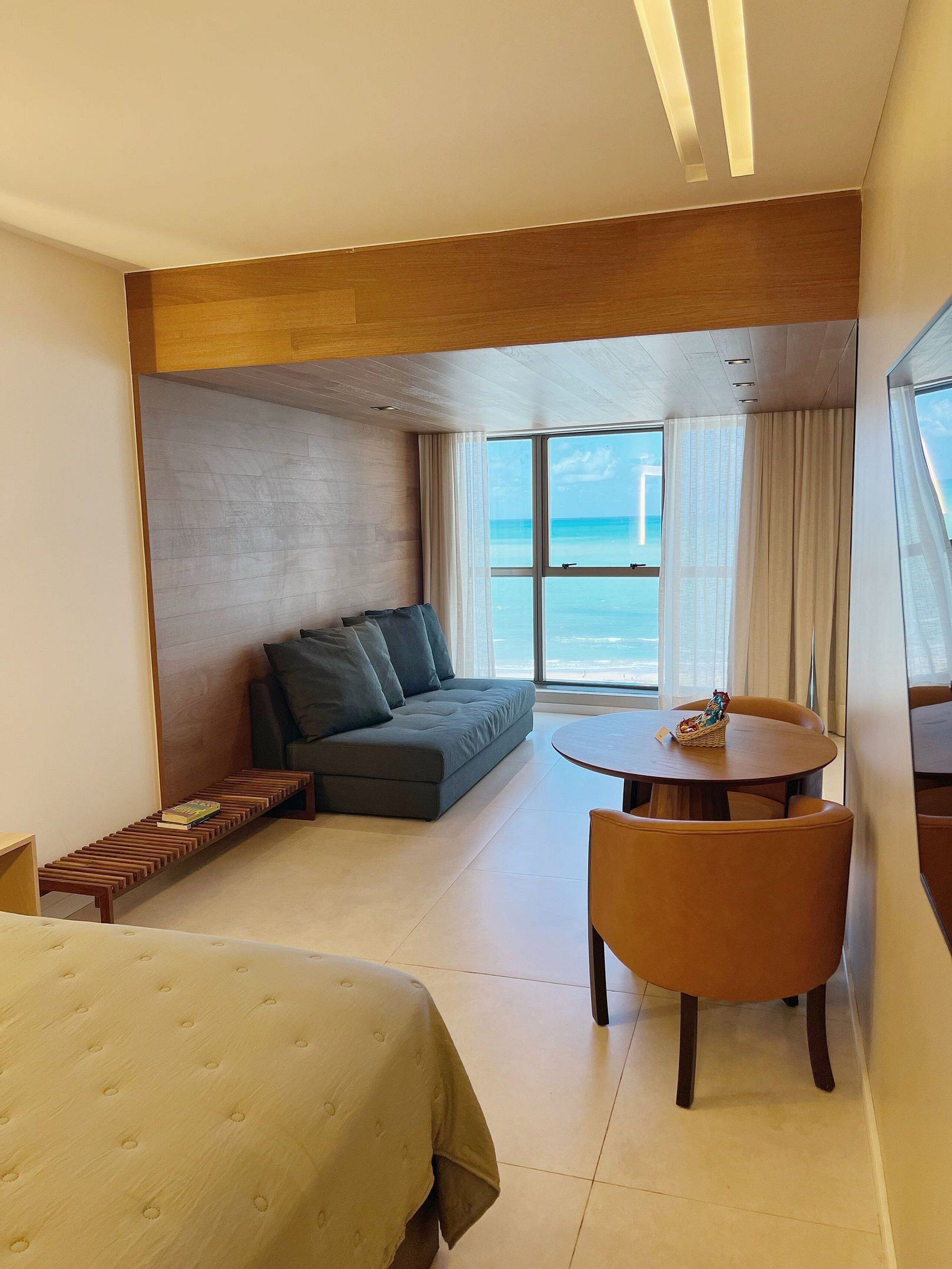 A modern hotel room with a sofa, a small round table, a bed, and a view of the ocean.