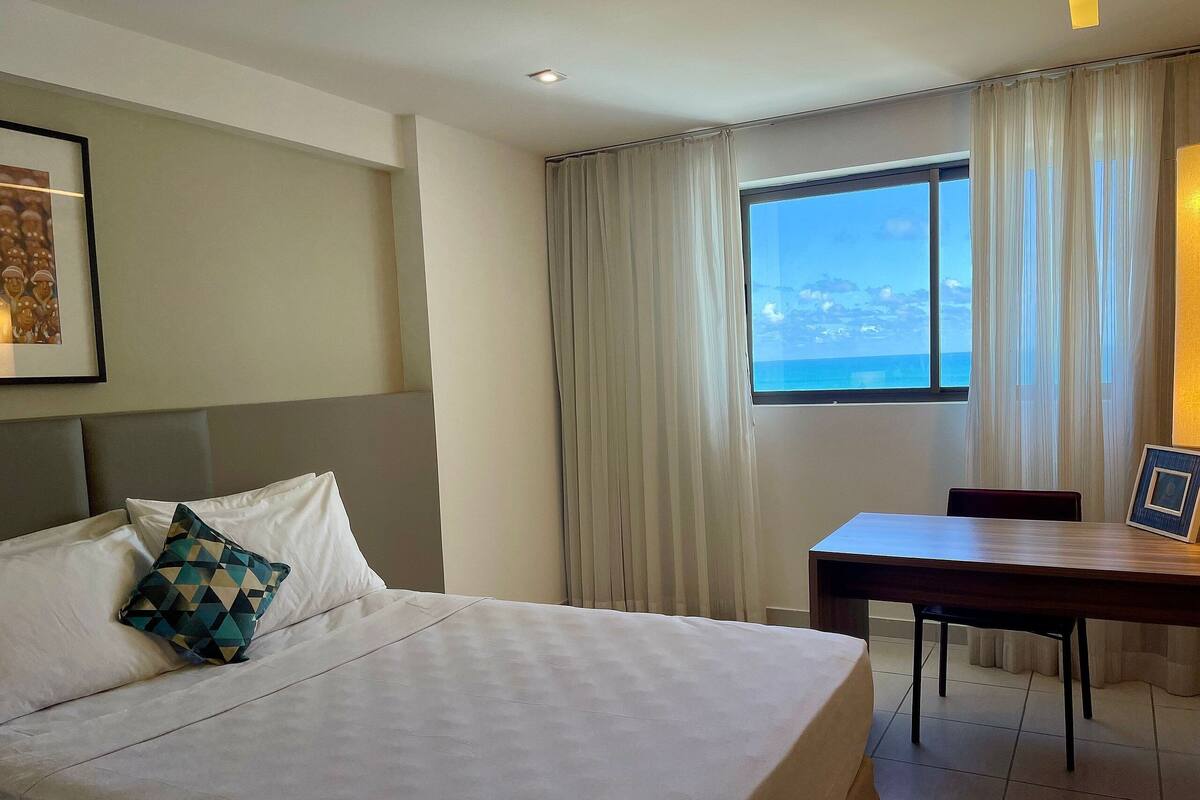 A hotel room with a bed, a desk, and a window with curtains.
