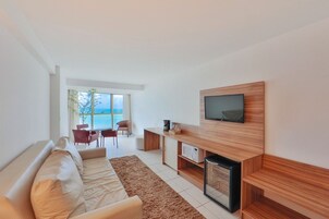 Una sala de estar moderna con sofá, televisor y mesa de centro. Se aprecia vista al exterior a través de grandes ventanales.