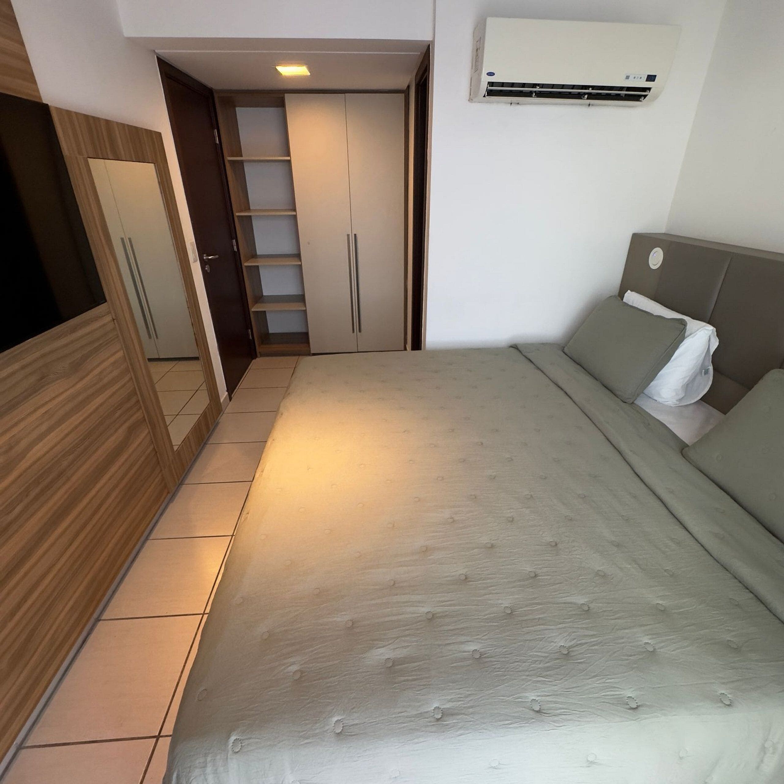 A bedroom with a bed, a wardrobe, a built-in shelf unit, and an air conditioning unit.