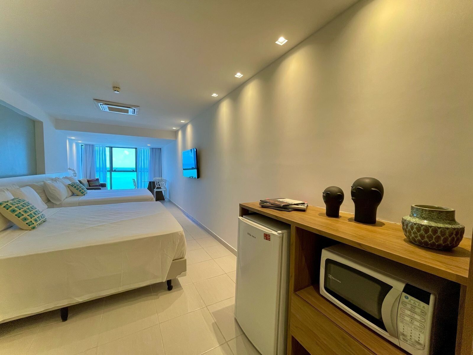 A hotel room with a bed, a desk with a microwave, and a refrigerator.
