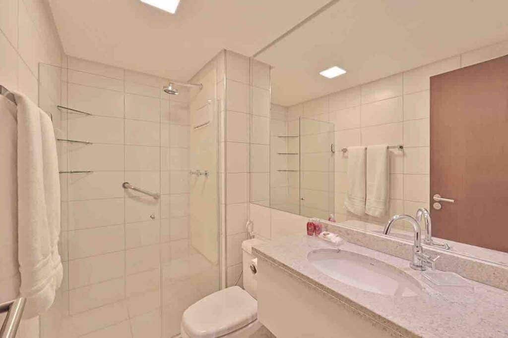 Um banheiro moderno com box de vidro, vaso sanitário branco, pia com espelho e porta-toalhas.