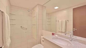 Um banheiro moderno com box de vidro, vaso sanitário branco, pia com espelho e porta-toalhas.