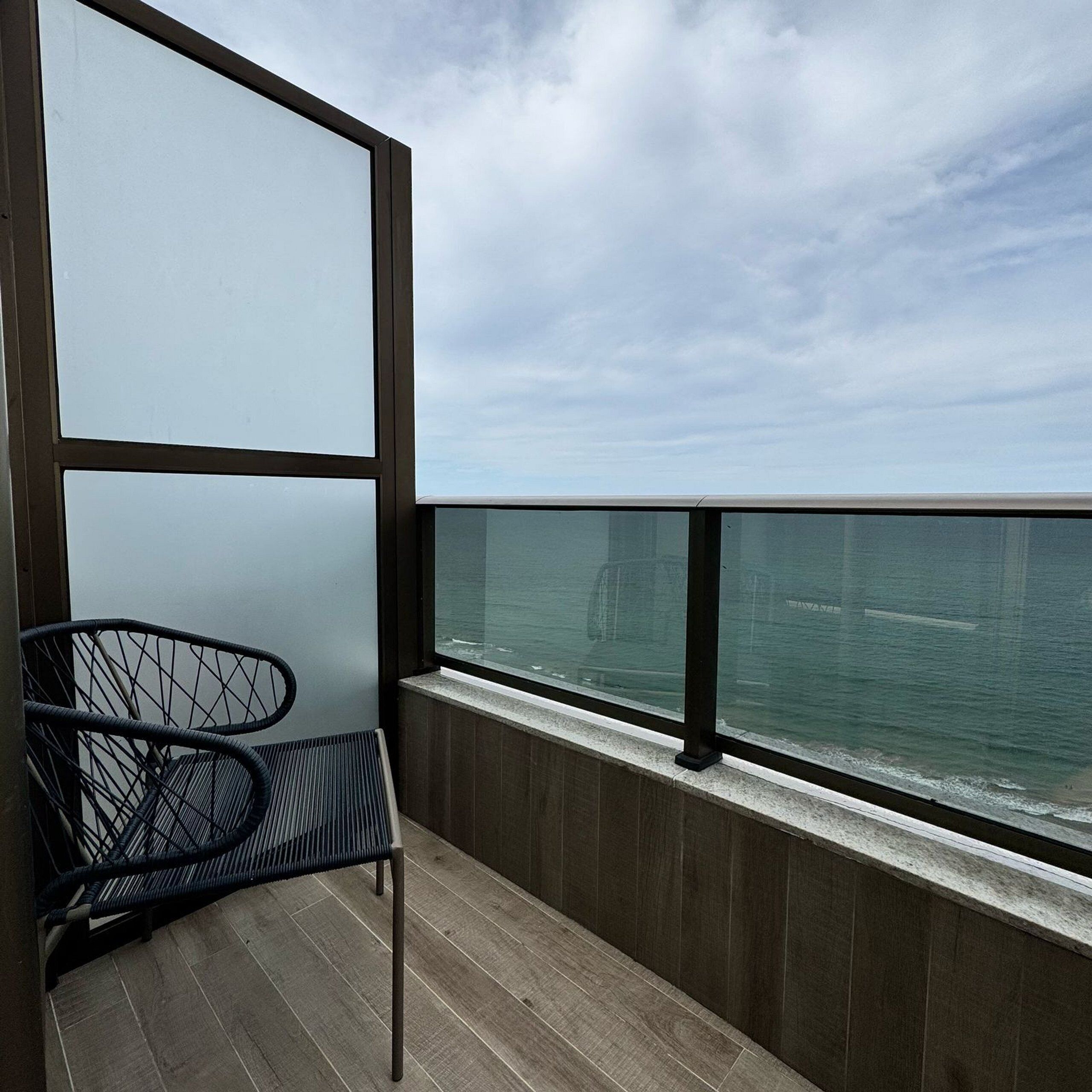 A balcony with a view of the sea, a chair, and a wooden floor.