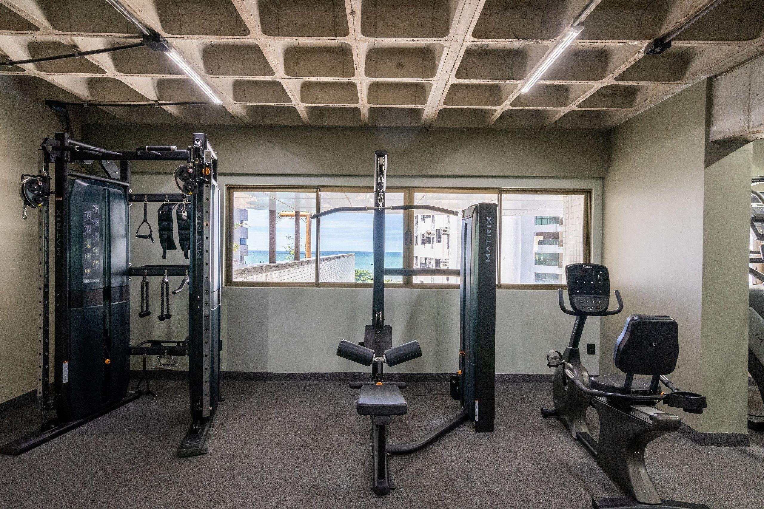 Ett gym med en knäböjsställning, en bänkpress och en crosstrainer.