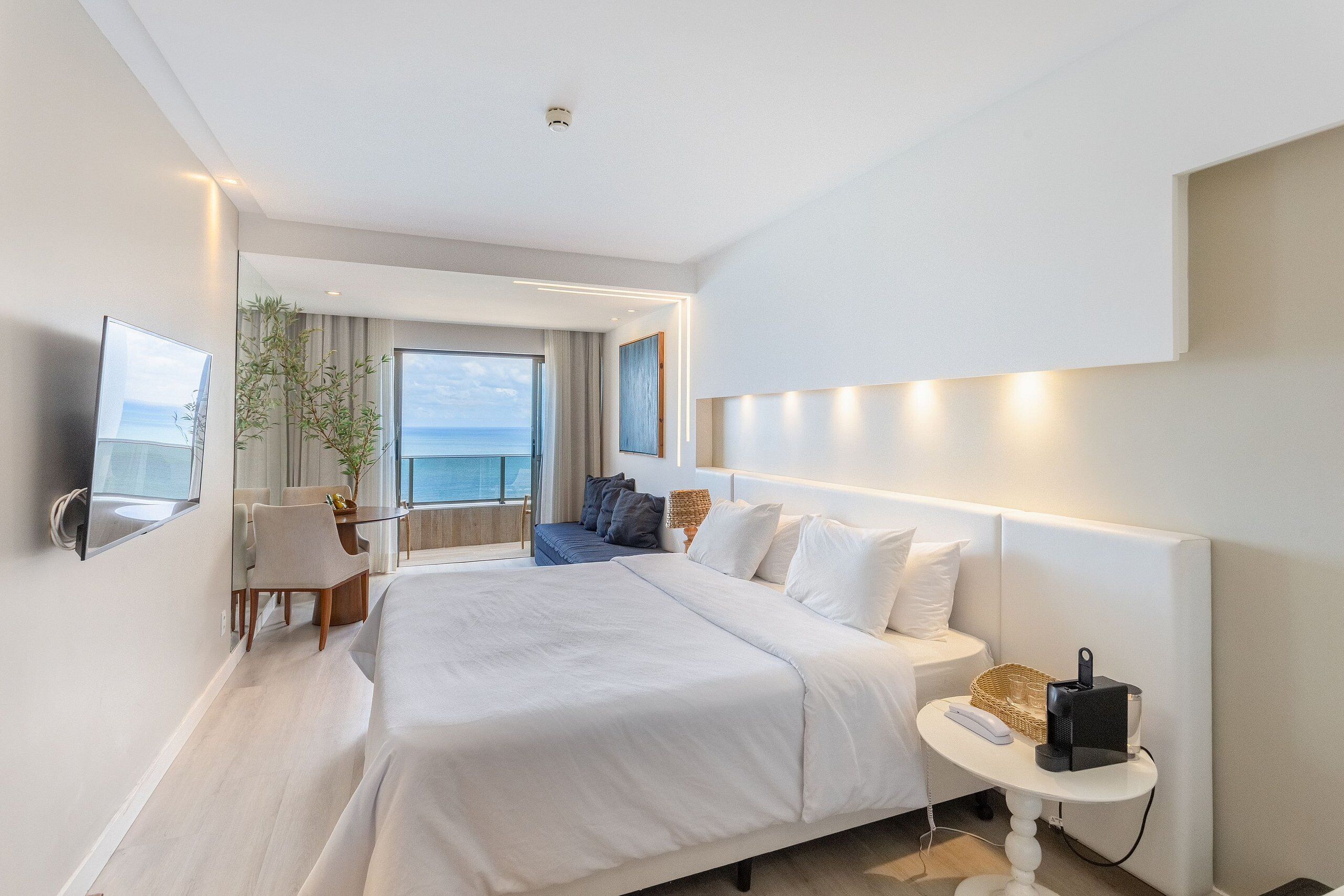 Camera d'albergo moderna con un letto grande, una scrivania, una sedia, una TV e vista sul mare.