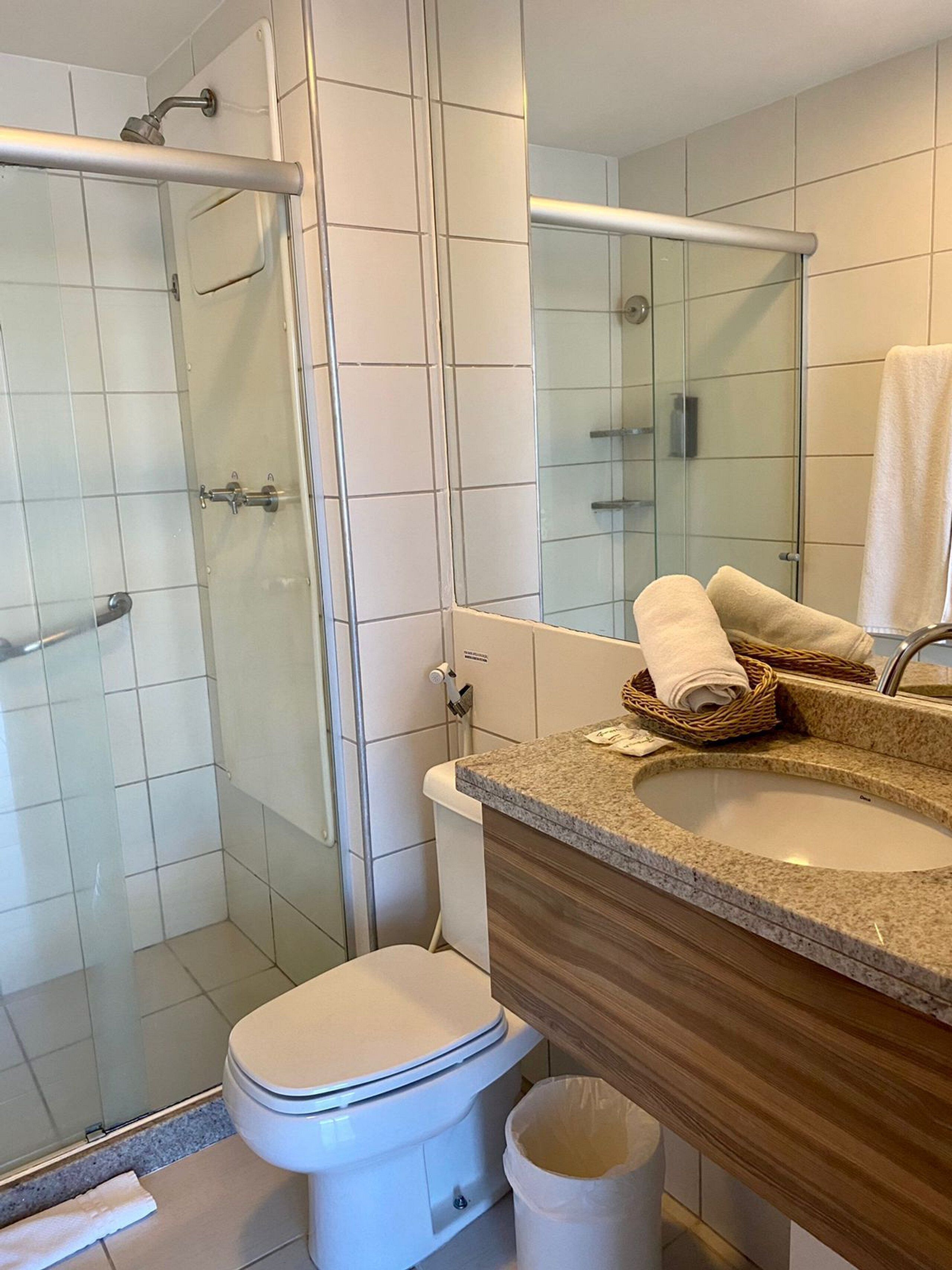 A modern bathroom with a glass shower enclosure, a white toilet, a granite sink, and a wooden vanity.