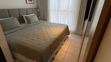 A bedroom with a large bed, a headboard, a framed picture on the wall, and a window with curtains.