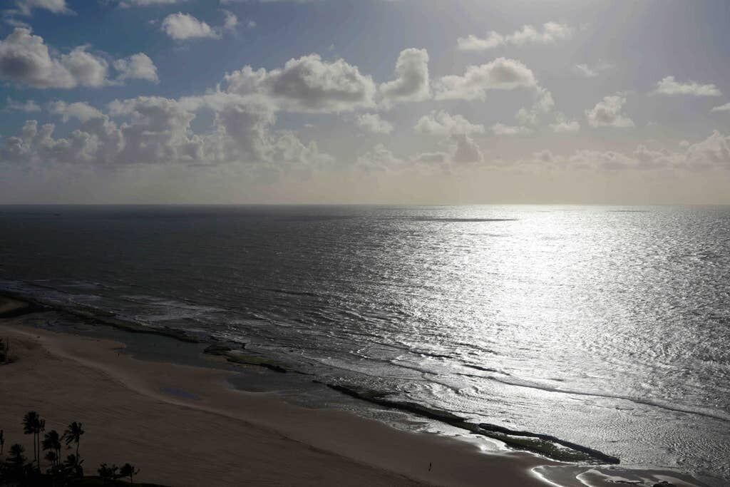 Uma praia com céu claro e luz do sol refletindo na água.