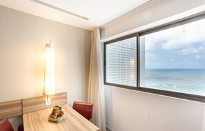 A hotel room with a wooden table, a red chair, a lamp, and a window with a view of the sea. - HY Beach Flats (Recife)