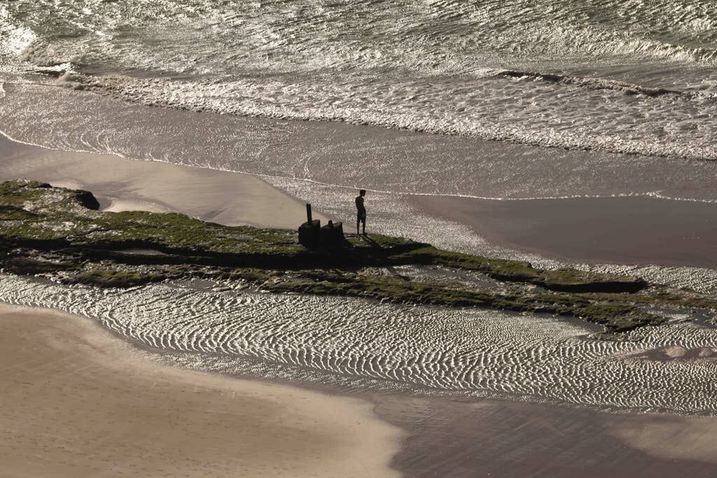 A beach with a person standing on a rock formation.