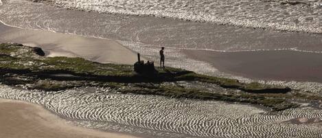 A beach with a person standing on a rock formation.