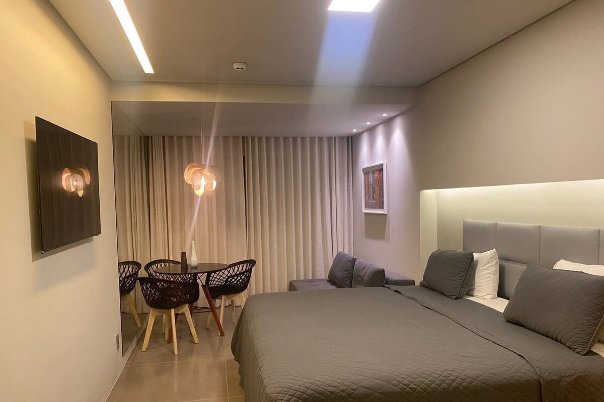 A modern hotel room with a large bed, a dining area with chairs, and a view of the city through the window.