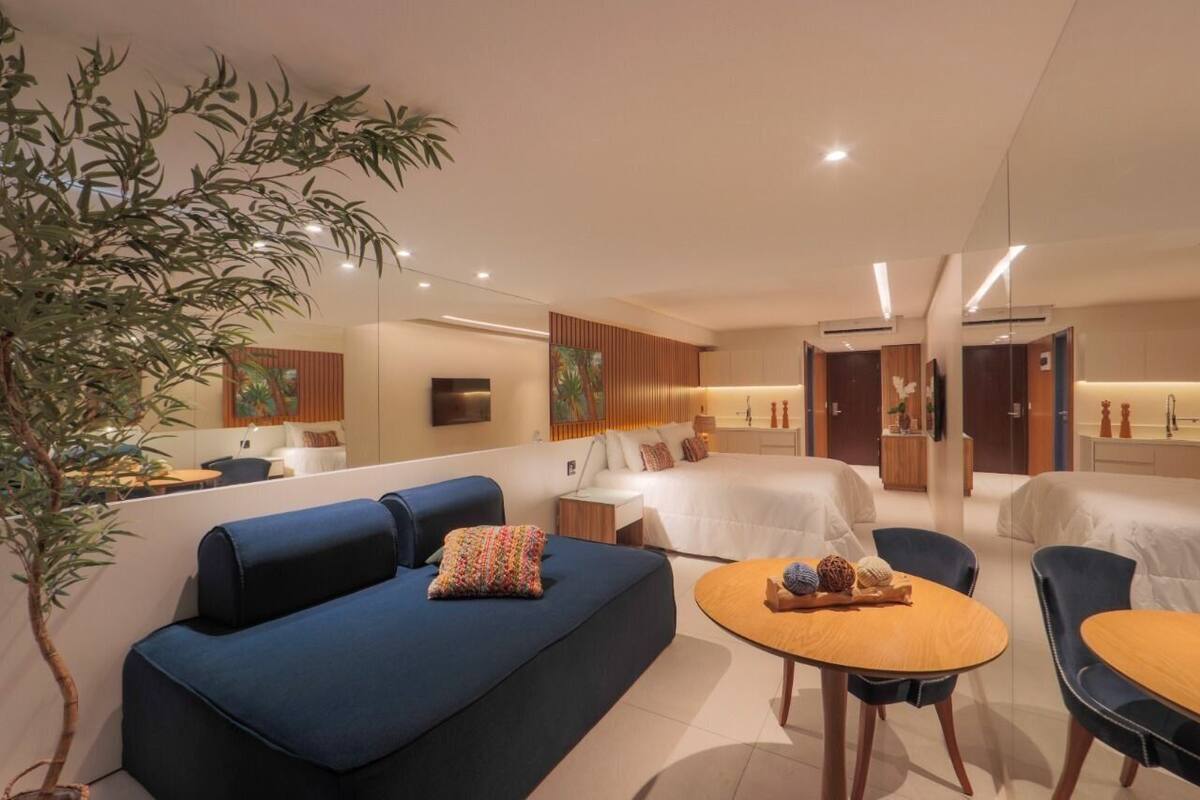 A modern hotel room with a blue sofa, a round wooden table, and a bed with white bedding.