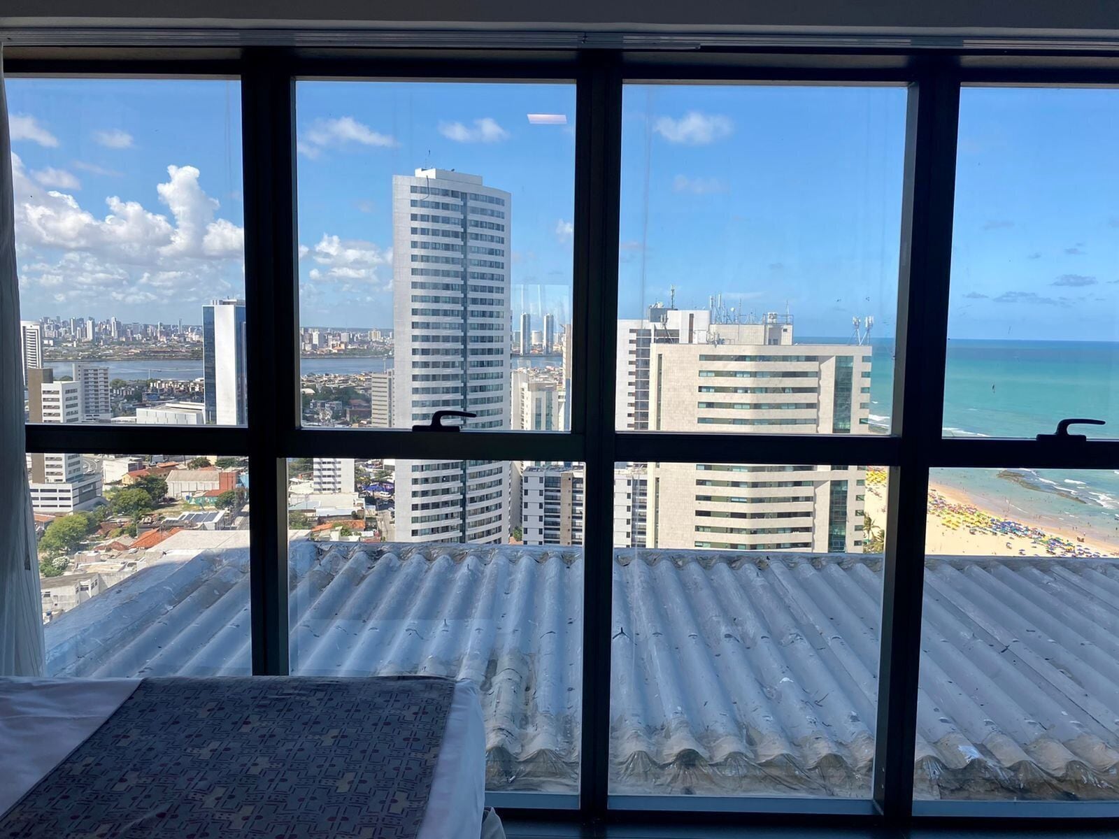 Quarto com uma janela grande com vista para um horizonte urbano e uma praia.