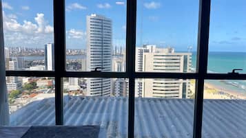Quarto com uma janela grande com vista para um horizonte urbano e uma praia.