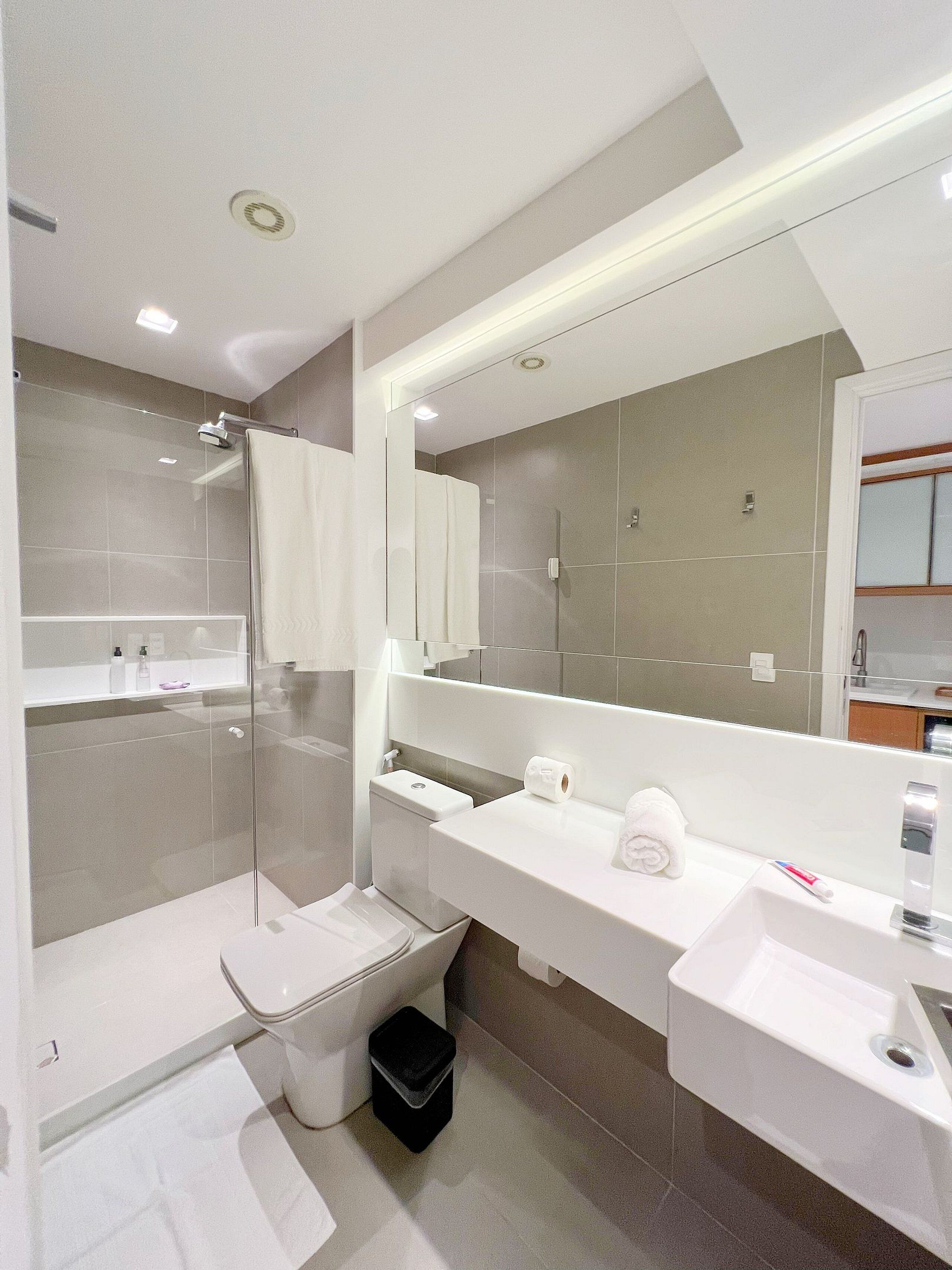 Un baño moderno con ducha de vidrio, inodoro, lavamanos y un espejo grande.