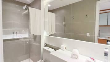 Un baño moderno con ducha de vidrio, inodoro, lavamanos y un espejo grande.