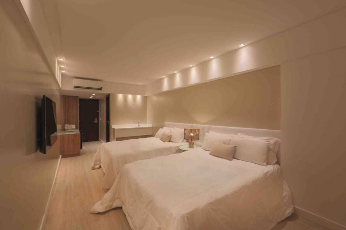 A hotel room with two beds, a wooden wardrobe, a mirror, and a small table.