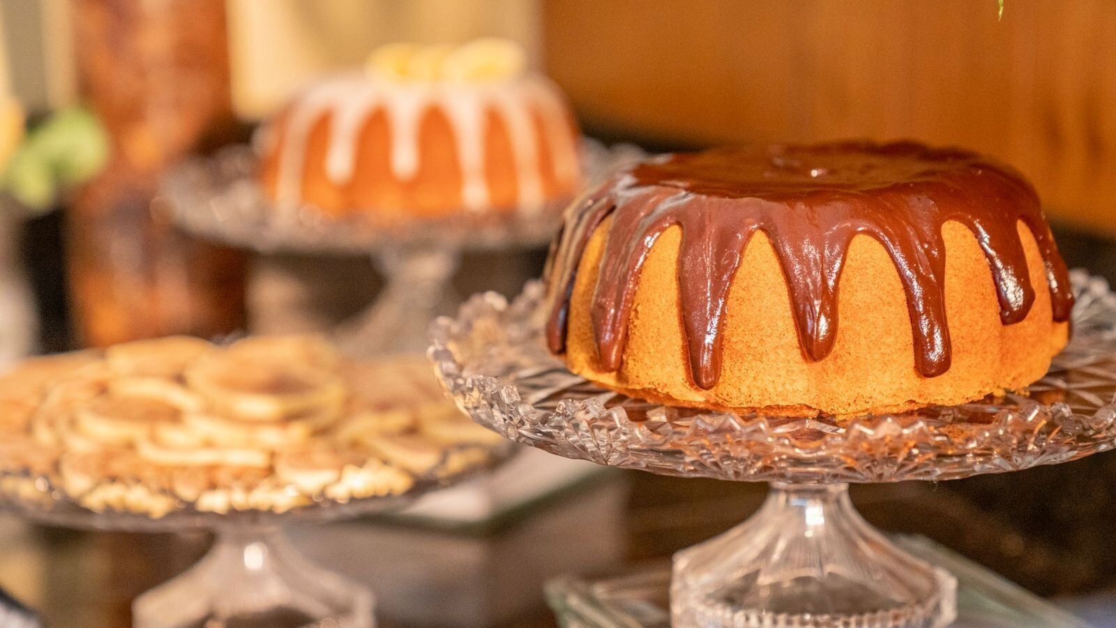 Um bolo bundt com cobertura de chocolate sobre um suporte de vidro.