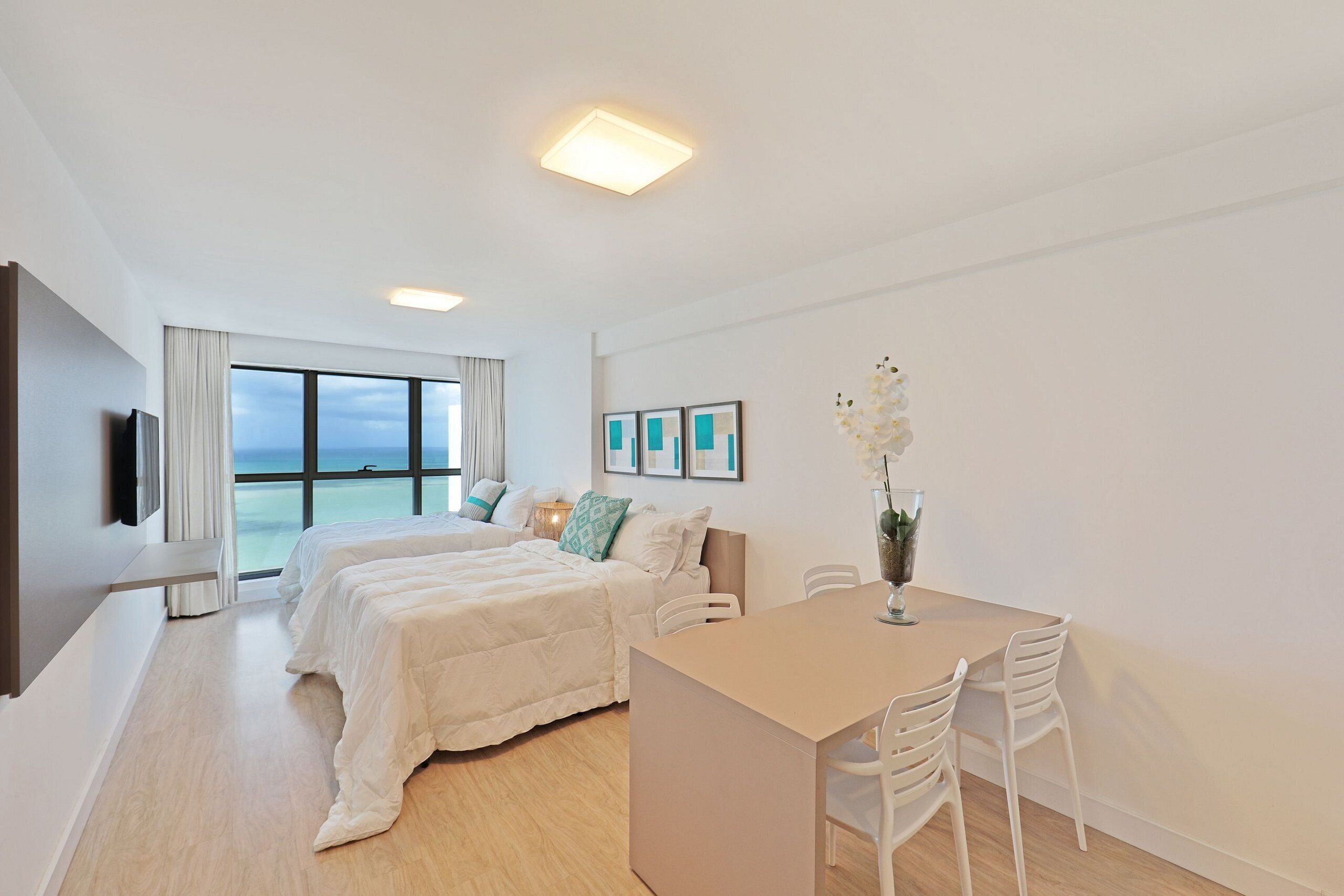 Une chambre d’hôtel moderne dotée d’un grand lit, d’un bureau avec des chaises, d’une télévision et offrant une vue sur la mer.