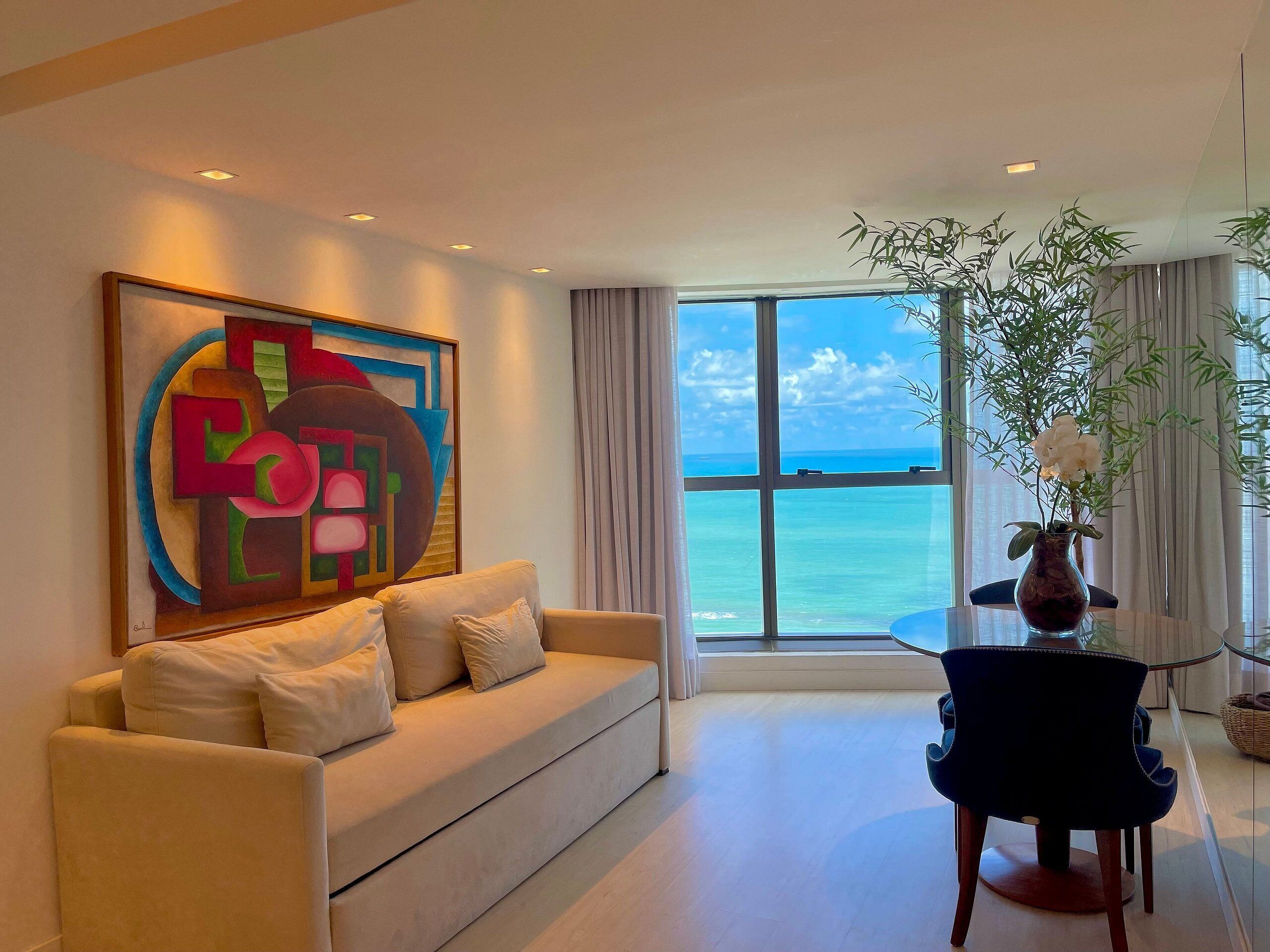 En moderne stue med et stort abstrakt maleri, en sofa, et spisebord og havudsigt.