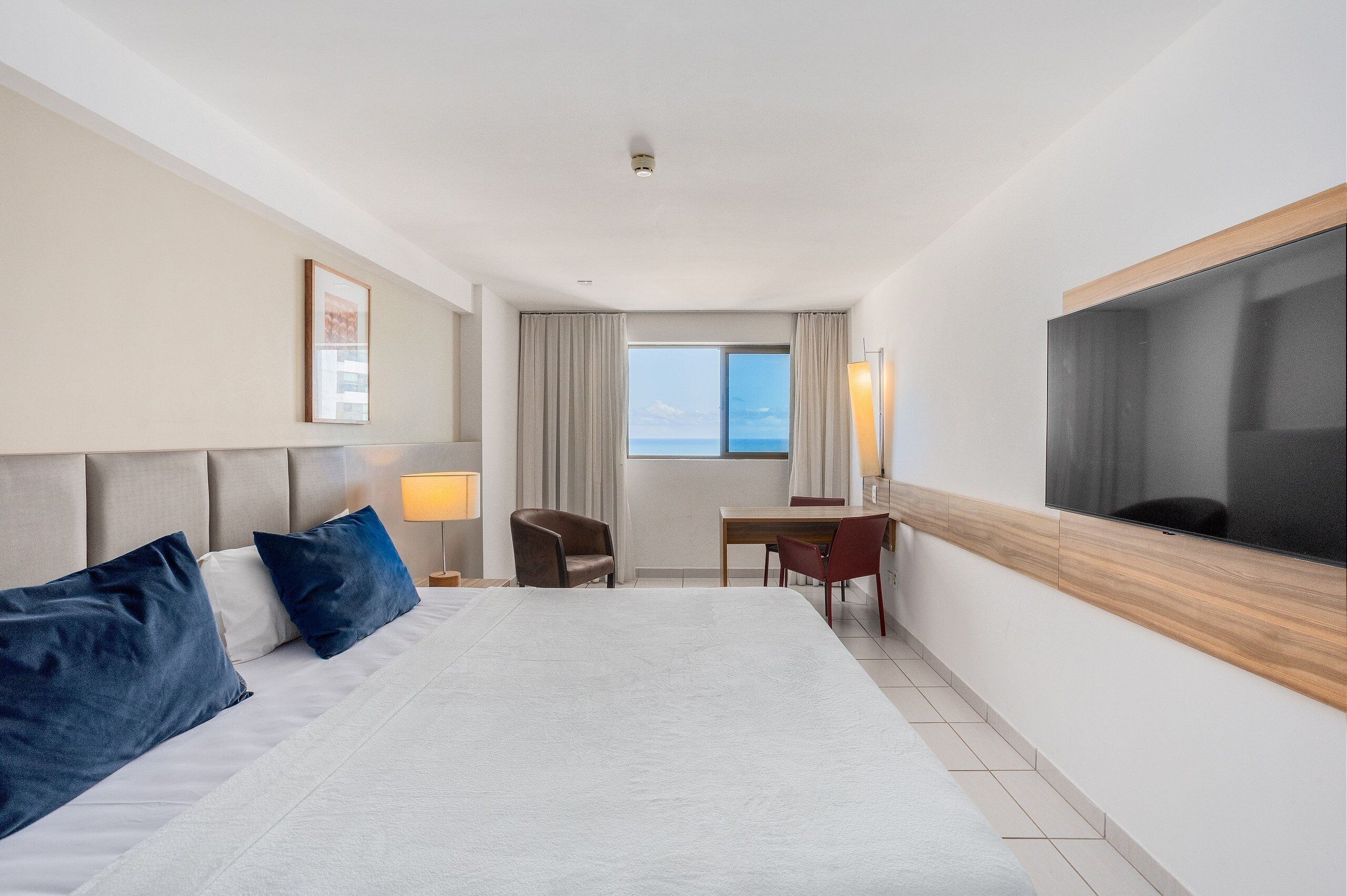Habitación de hotel con una cama grande, un escritorio, una silla, un televisor y vista al mar.