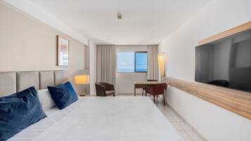 Habitación de hotel con una cama grande, un escritorio, una silla, un televisor y vista al mar.