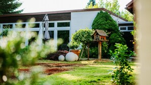 A modern house with a well-maintained garden, including a lawn, a birdhouse, and a patio umbrella. - Hotel Hasselhof Superior (Braunlage)