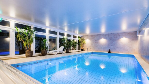 An indoor swimming pool with clear blue tiles, potted plants, and a sun lounger. - Hotel Hasselhof Superior (Braunlage)