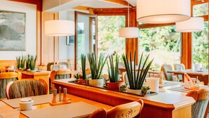 A restaurant with wooden furniture, potted plants, and hanging lamps. - Hotel Hasselhof Superior (Braunlage)