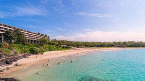 Un hotel a la vora de la platja, amb aigües turqueses cristal·lines, sorra daurada i vegetació exuberanta.
