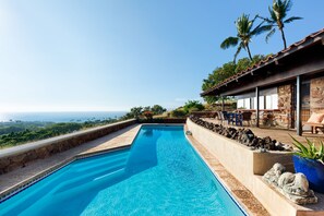 Une piscine avec vue sur l’océan, des murs en pierre et un espace salon extérieur.