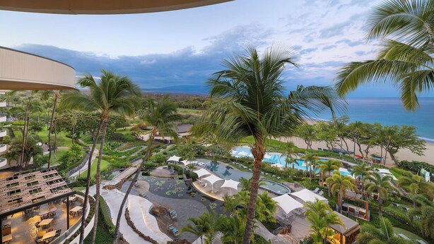 Un complex turístic amb zona de piscina, palmeres i vista a l'oceà.