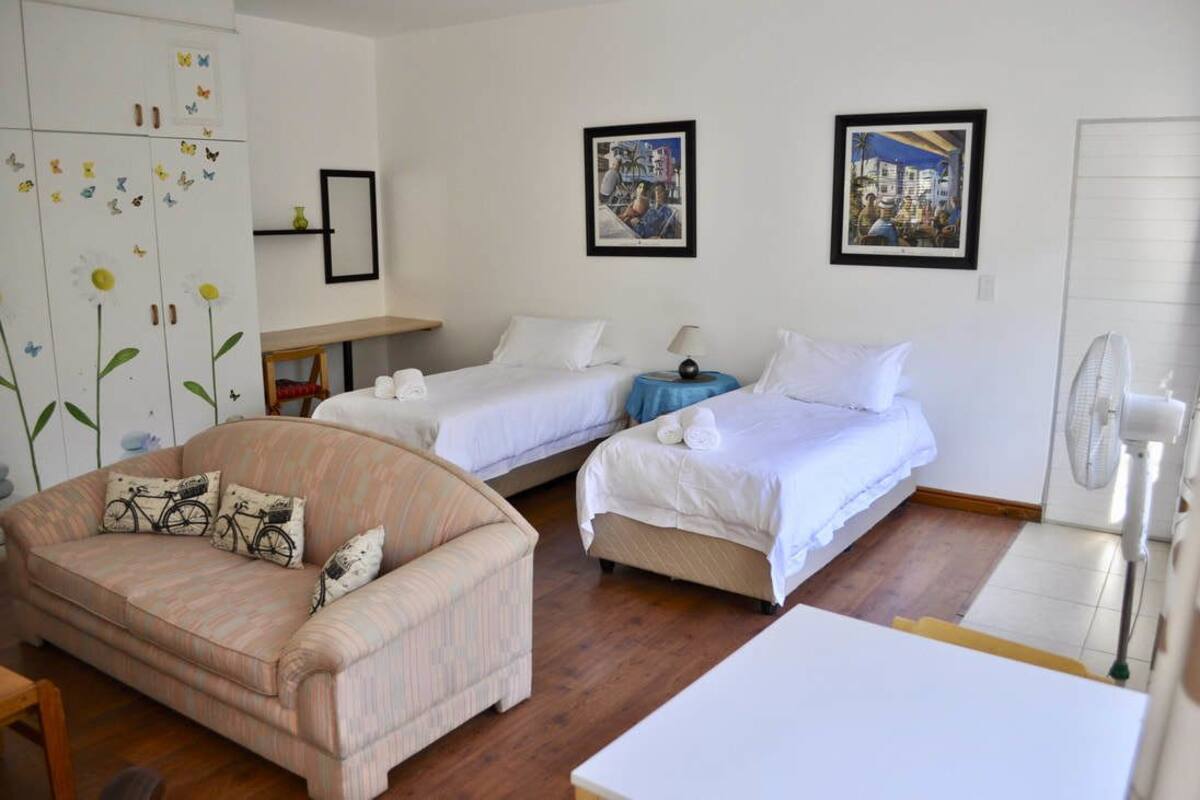 A hotel room with two single beds, a sofa, a small table, and a fan.
