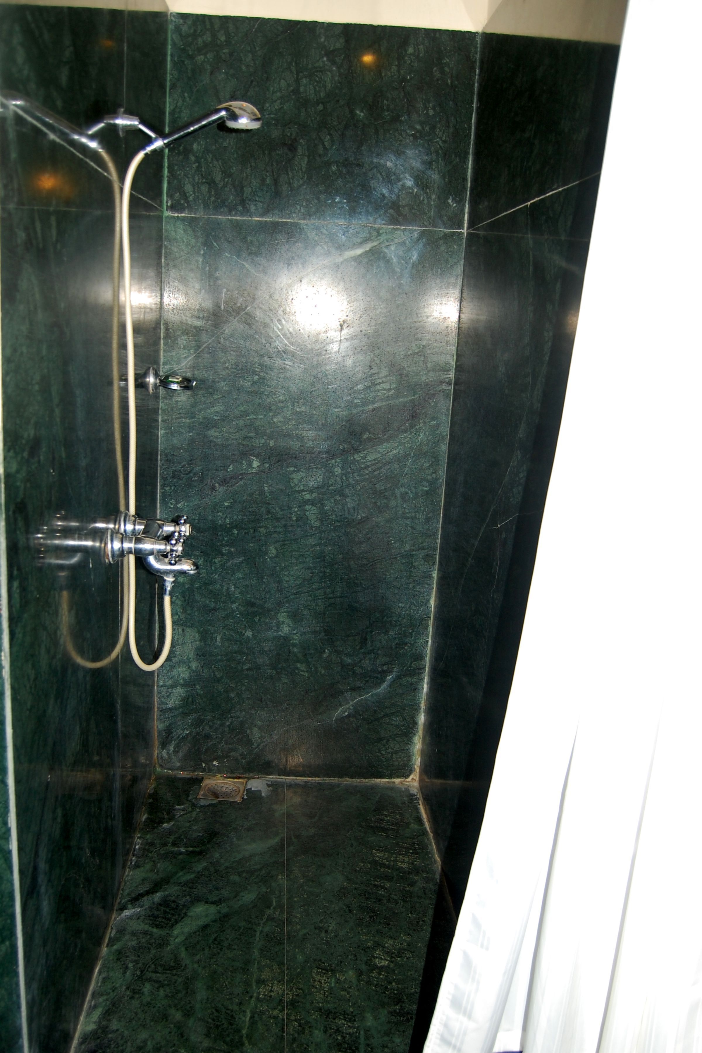 Casa de banho com paredes de mármore escuro, chuveiro com um duche manual e um porta-toalhas.