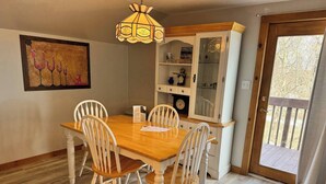 Un comedor con mesa de madera y sillas blancas, una araña y un mueble con puertas de cristal.